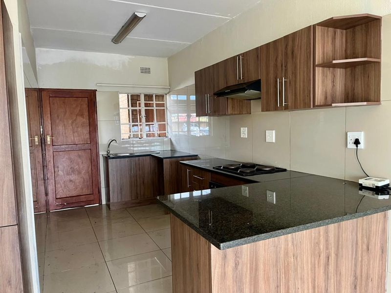 Modern kitchen featuring wood-finish cabinetry, granite countertops, an electric hob, and tiled flooring, offering a functional and clean workspace.