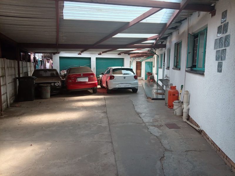 A covered carport area featuring concrete flooring, double garage doors, and an external utility sink attached to the main building structure.