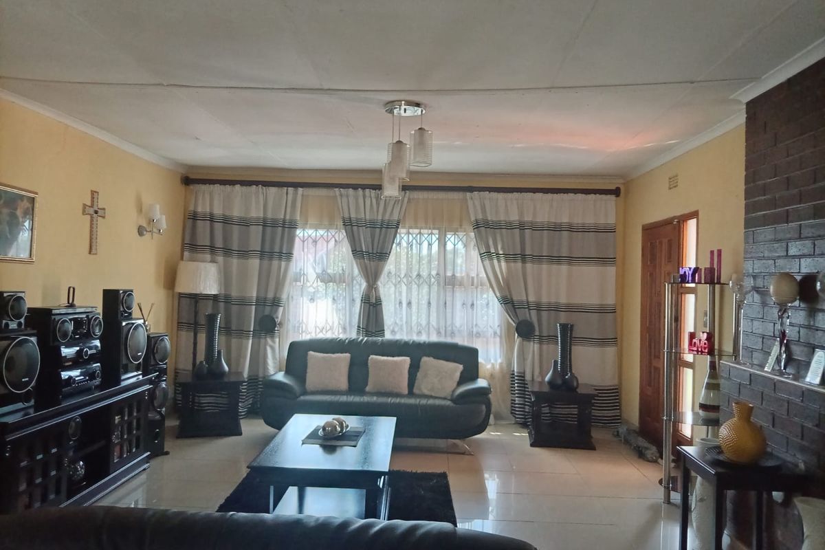 A comfortable living room featuring tiled flooring, a prominent brick fireplace, and large windows with security gates, offering a functional and inviting space.