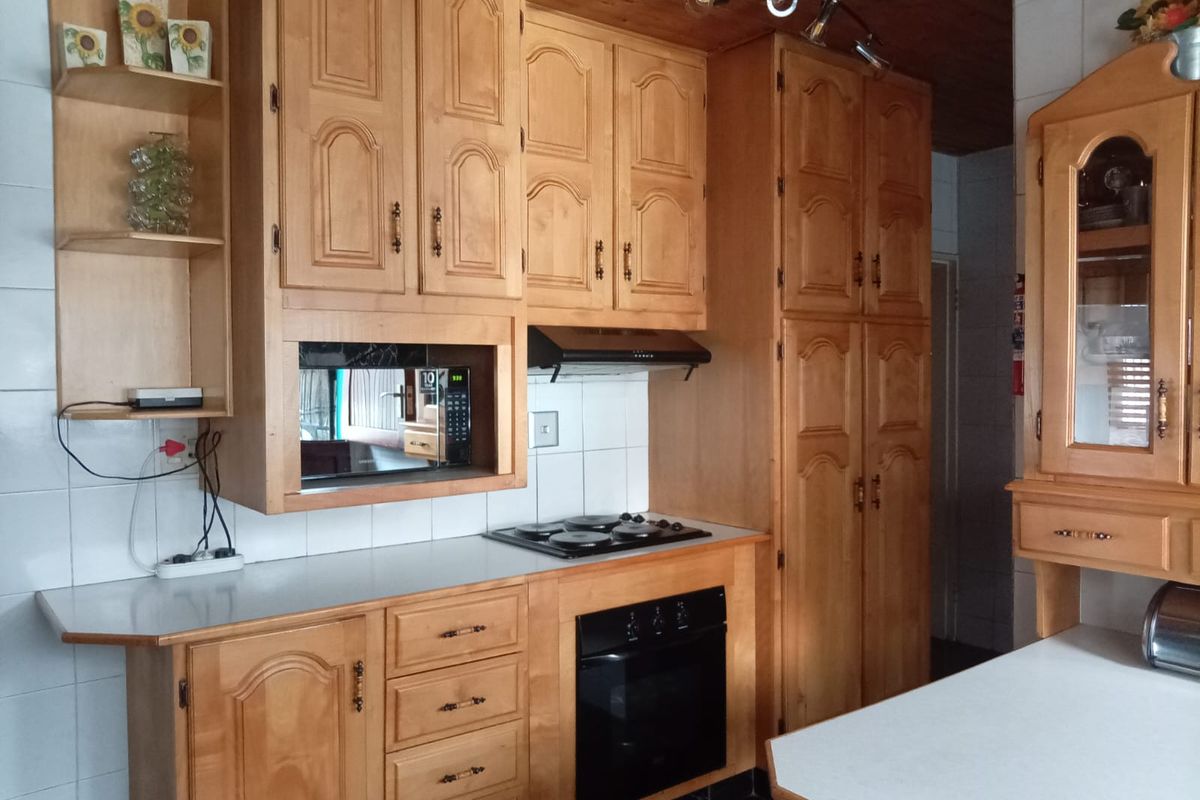 A traditional kitchen featuring extensive wooden cabinetry, built-in oven, electric hob, extractor fan, and tiled splashbacks with a timber ceiling.