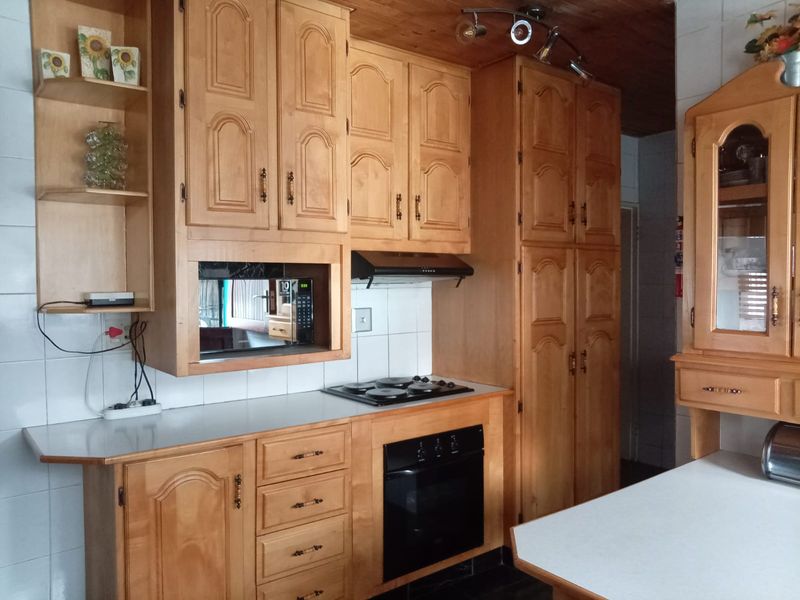 A traditional kitchen featuring extensive wooden cabinetry, built-in oven, electric hob, extractor fan, and tiled splashbacks with a timber ceiling.