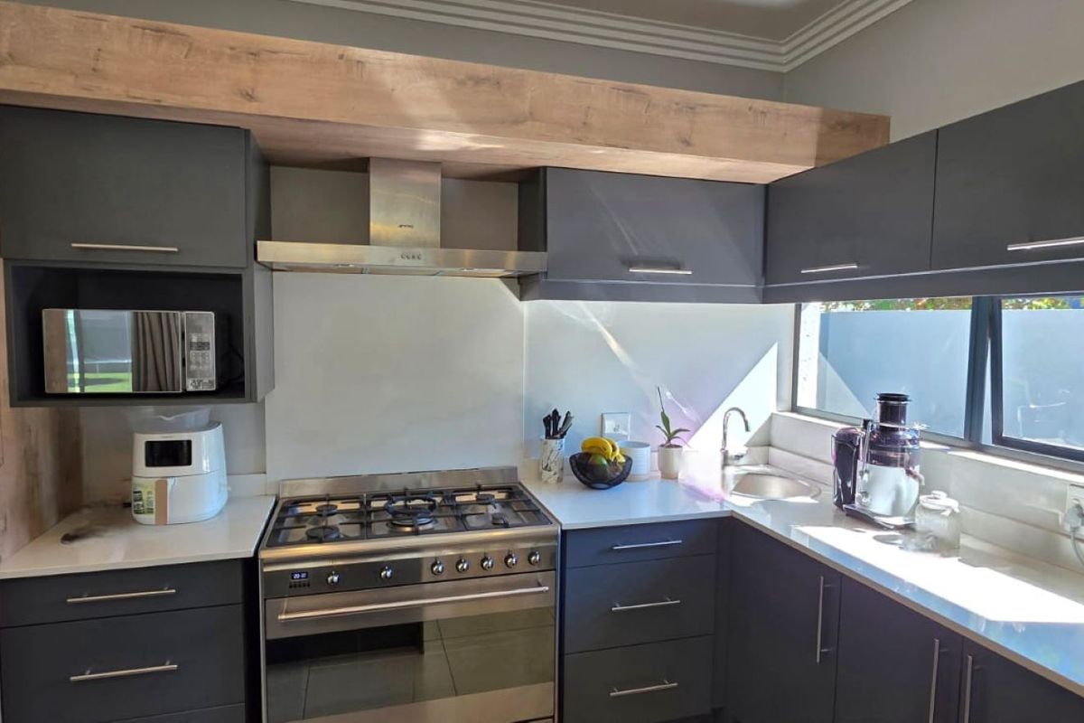 Modern kitchen featuring dark grey cabinetry, light wood-look bulkhead, quartz countertops, gas hob, extractor fan, and integrated microwave.