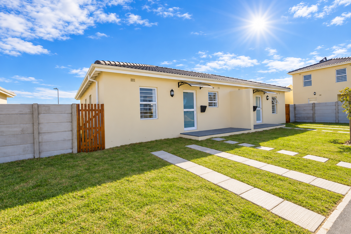 A well-maintained single-story residential property featuring a paved driveway, neat lawn, concrete boundary wall, and modern exterior finishes under a clear sky.