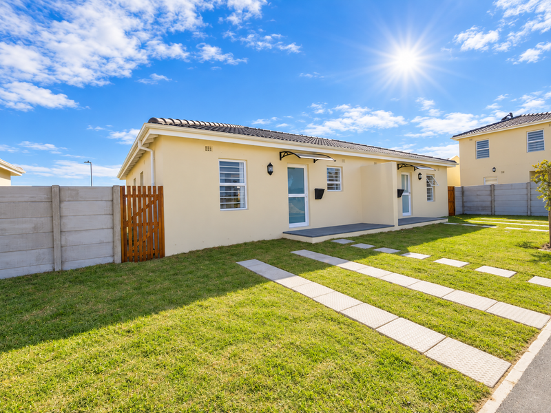 A well-maintained single-story residential property featuring a paved driveway, neat lawn, concrete boundary wall, and modern exterior finishes under a clear sky.