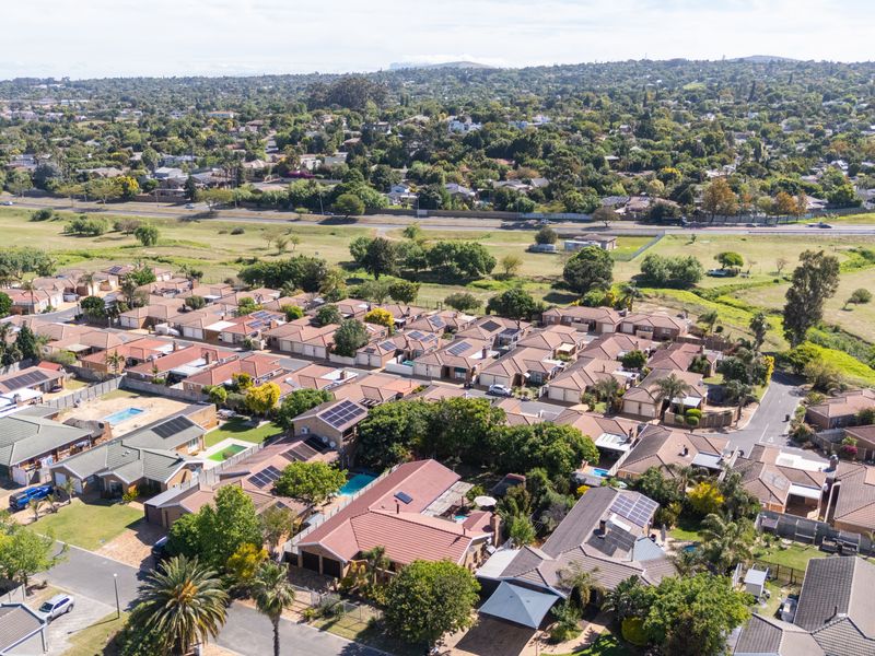 An aerial view of a residential suburban neighborhood featuring multiple houses with tiled roofs, solar panels, and private swimming pools.