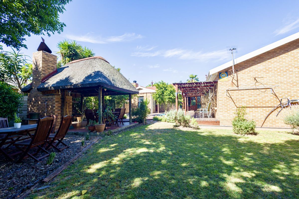 Spacious rear garden featuring a traditional thatched lapa with a built-in brick fireplace, a wooden pergola, and well-maintained lawn area.