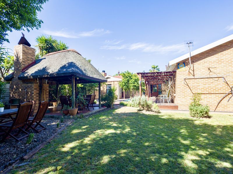 Spacious rear garden featuring a traditional thatched lapa with a built-in brick fireplace, a wooden pergola, and well-maintained lawn area.