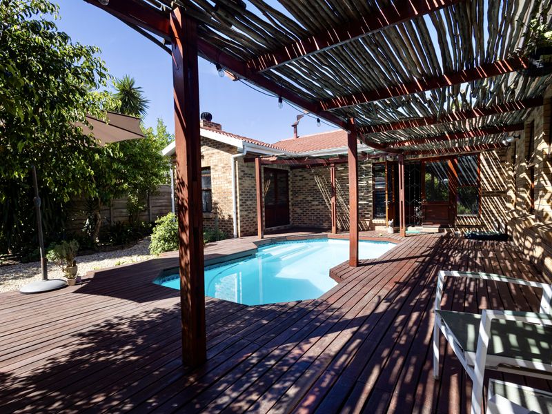 Outdoor entertainment area featuring a swimming pool, timber decking, and a rustic timber pergola attached to the brick house exterior.