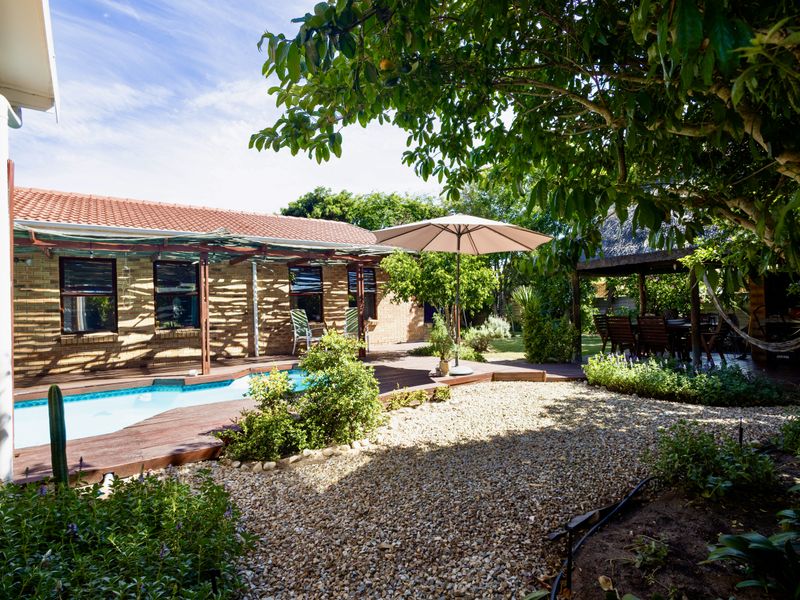 A well-maintained outdoor area featuring a swimming pool, timber decking, and a thatched gazebo set within a landscaped garden.