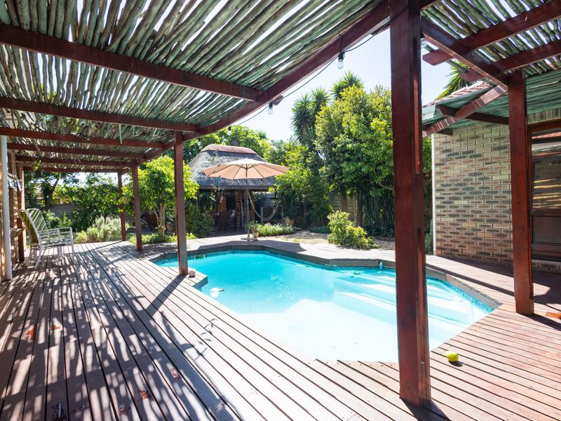 Outdoor pool area featuring a wooden deck, timber pergola structure, and a swimming pool set within a landscaped garden.