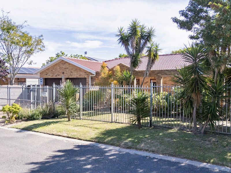 Front view of a single-story brick house featuring a tiled roof, double garage, and secure metal perimeter fencing with established garden landscaping.