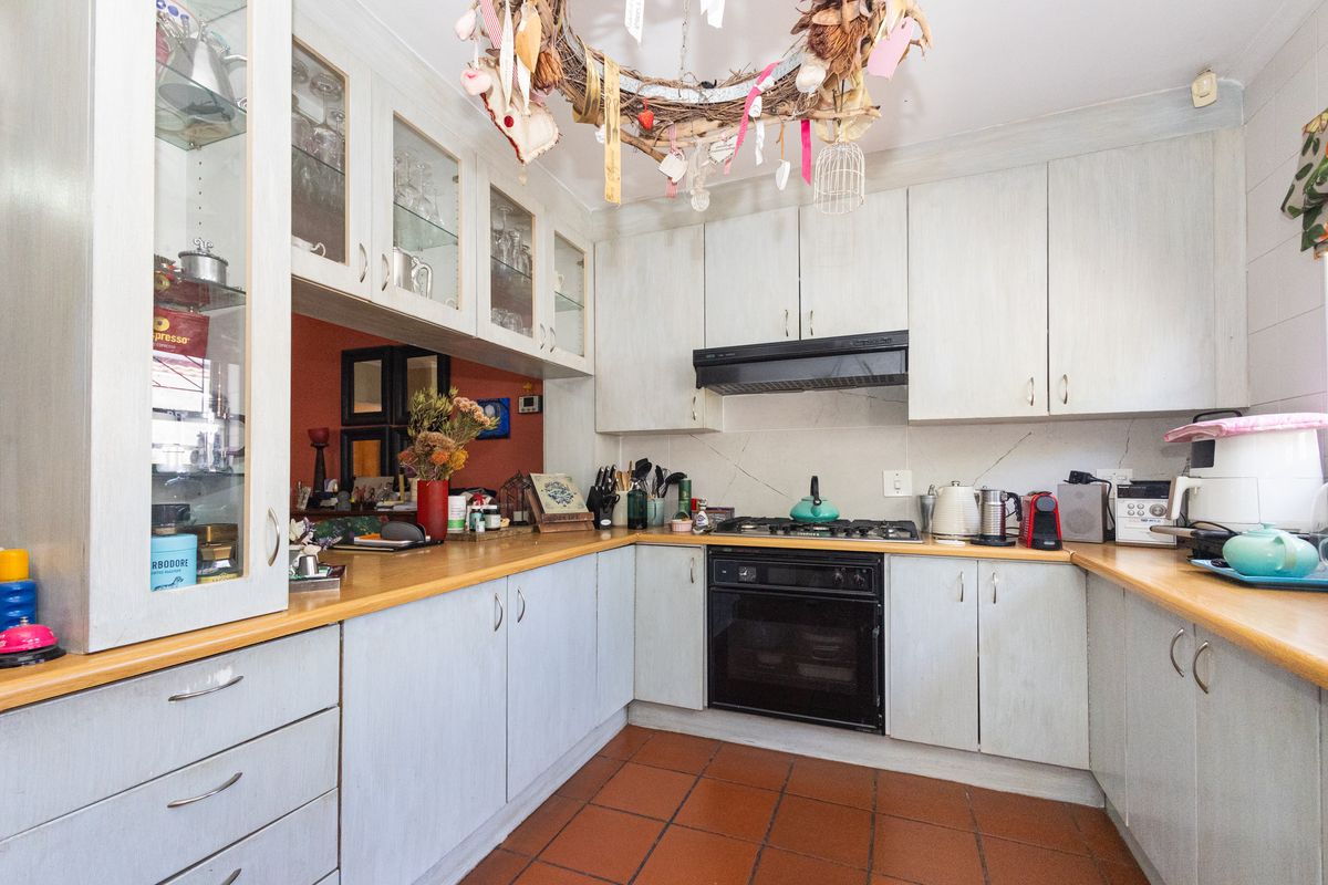 A functional kitchen featuring light-toned cabinetry, laminate countertops, a gas hob, and a built-in oven, finished with traditional terracotta-style floor tiles.