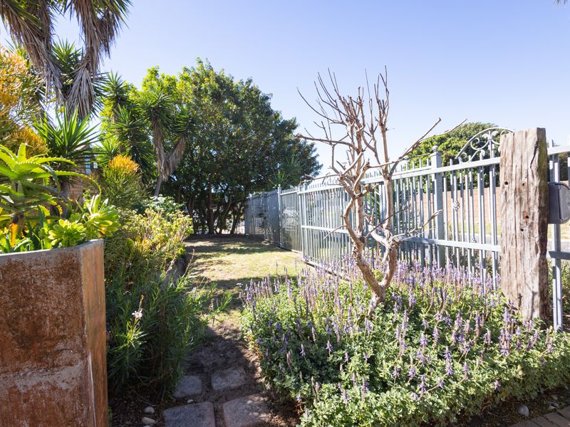 A well-maintained garden area featuring established landscaping, stone paving, and secure metal perimeter fencing.