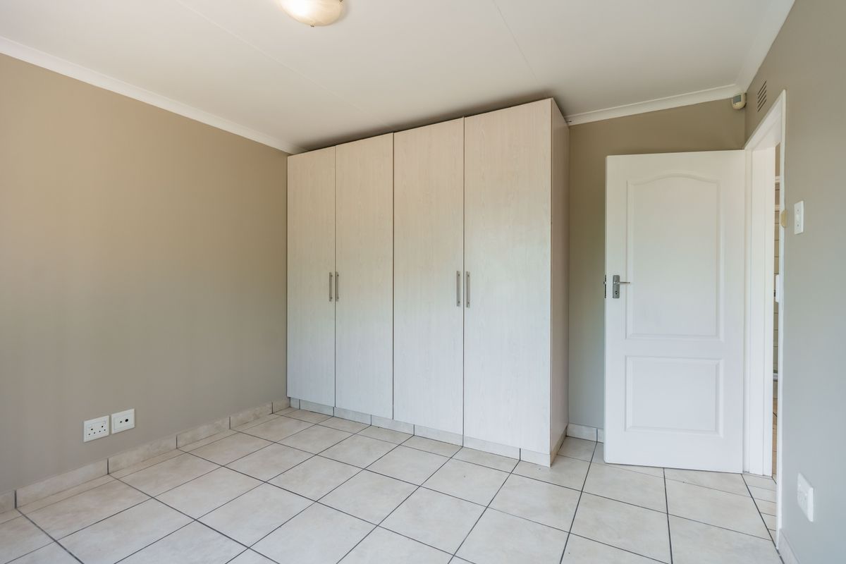 A clean, empty bedroom featuring neutral wall tones, tiled flooring, and ample built-in cupboard storage space.