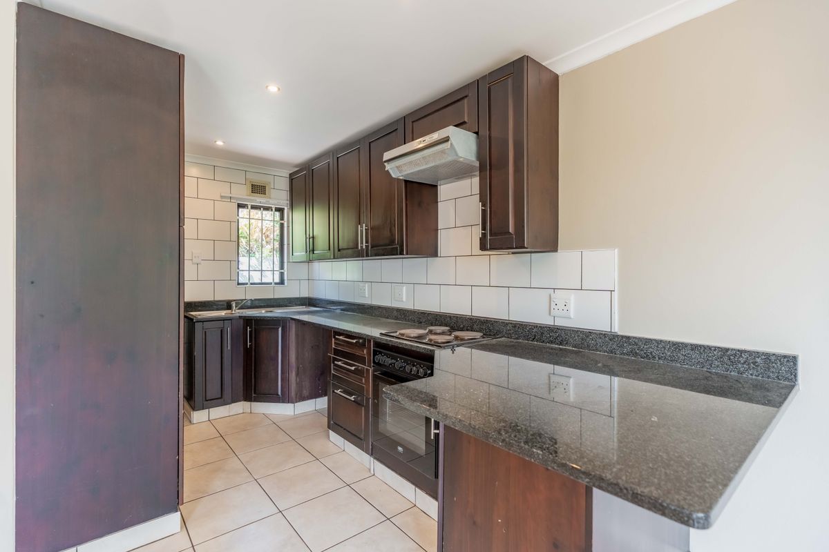 A clean, functional kitchen featuring dark wood cabinetry, granite countertops, built-in oven, electric hob, and a modern subway tile backsplash.