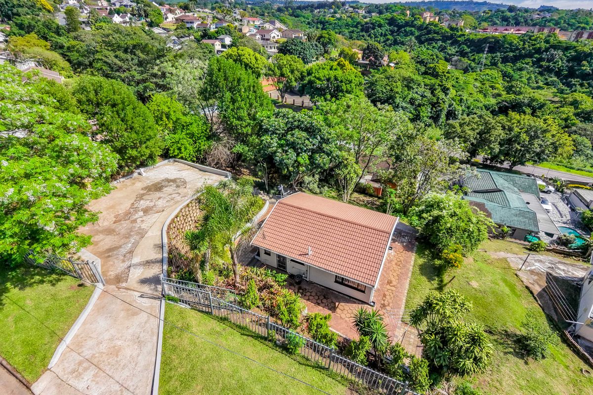 Aerial view of a residential property featuring a tiled roof house, paved driveway, and established garden set within a suburban landscape.