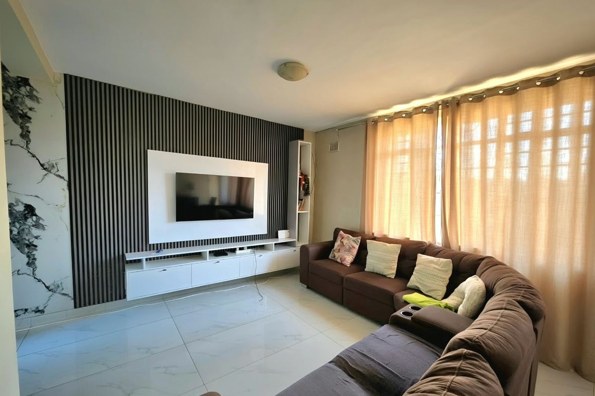A modern living room featuring a stylish slatted feature wall, built-in media console, marble-effect wall accents, and polished tiled flooring.