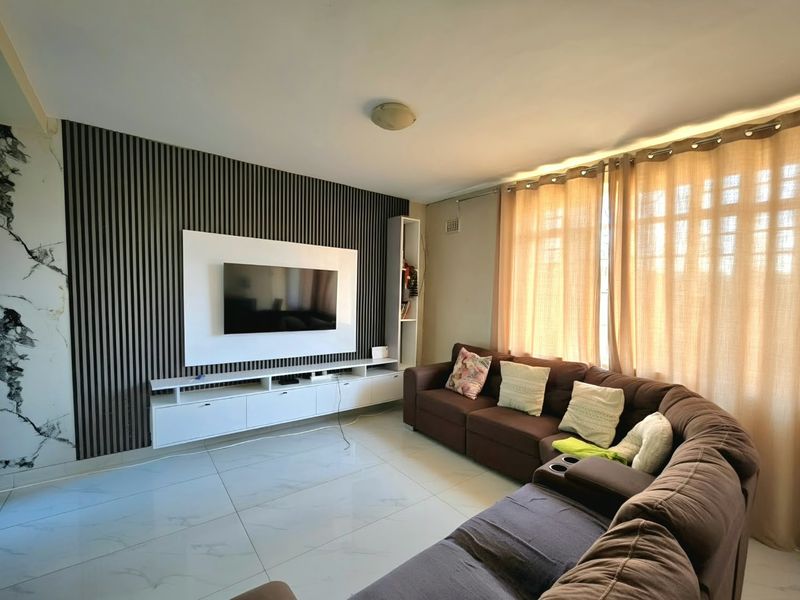A modern living room featuring a stylish slatted feature wall, built-in media console, marble-effect wall accents, and polished tiled flooring.