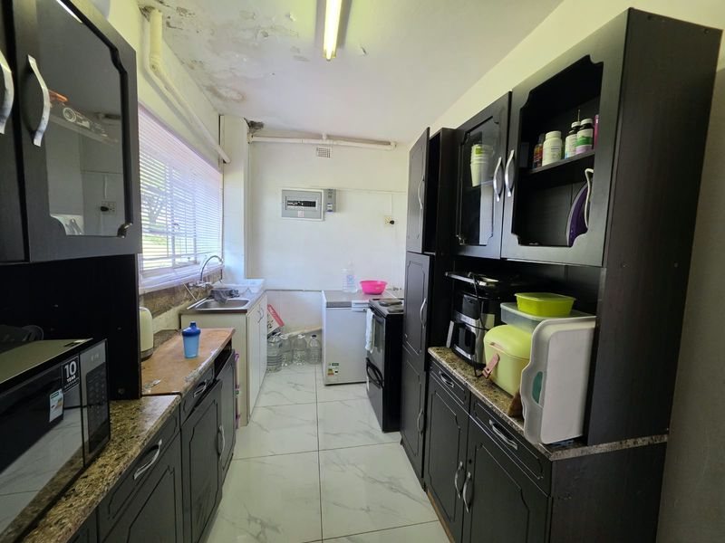 A compact kitchen featuring dark cabinetry, tiled flooring, and a stainless steel sink, currently showing signs of ceiling water damage and wear.