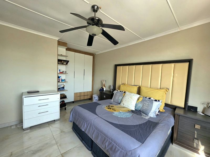A well-maintained bedroom featuring tiled flooring, a ceiling fan, and a built-in wardrobe with integrated shelving.