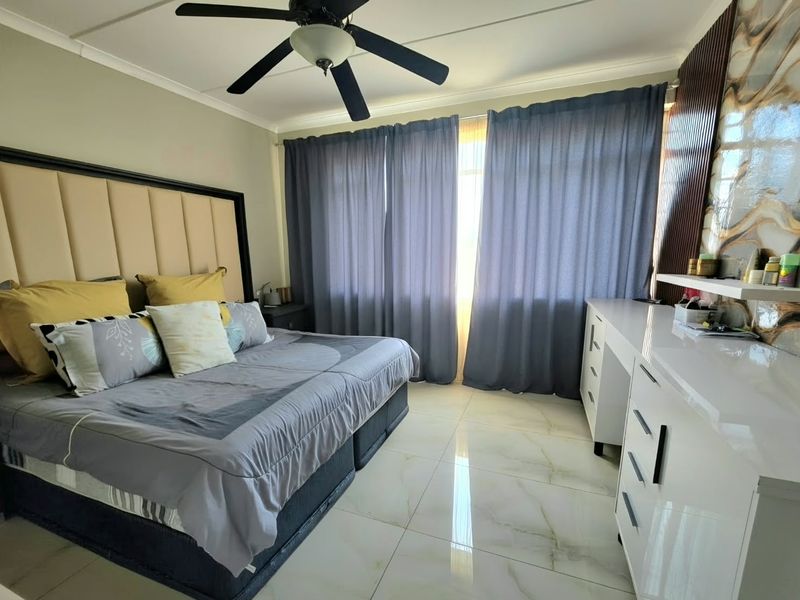 Spacious bedroom featuring polished porcelain floor tiles, a ceiling fan, and a modern built-in vanity unit with decorative wall accents.