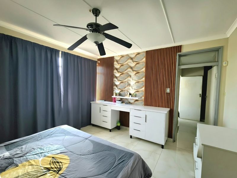 A well-maintained bedroom featuring a ceiling fan, tiled flooring, and a modern built-in vanity unit with decorative slatted wood wall paneling.