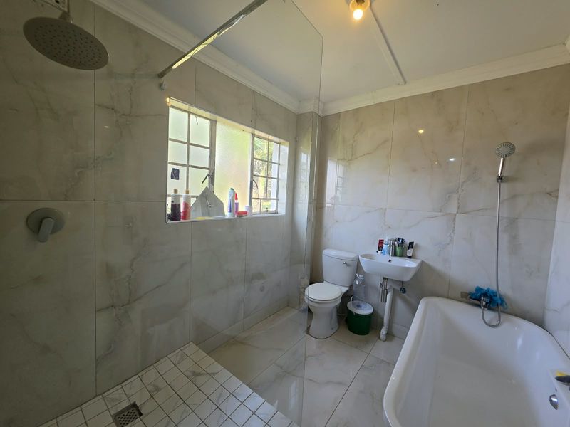 Modern bathroom featuring a walk-in shower with glass screen, rainfall shower head, freestanding bathtub, wall-mounted toilet, and basin with marble-look tiling throughout.