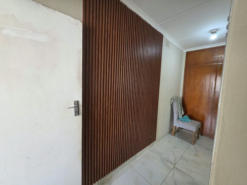 Hallway featuring decorative slatted wood wall paneling, built-in wooden storage cupboards, and tiled flooring, showing signs of wall surface wear.
