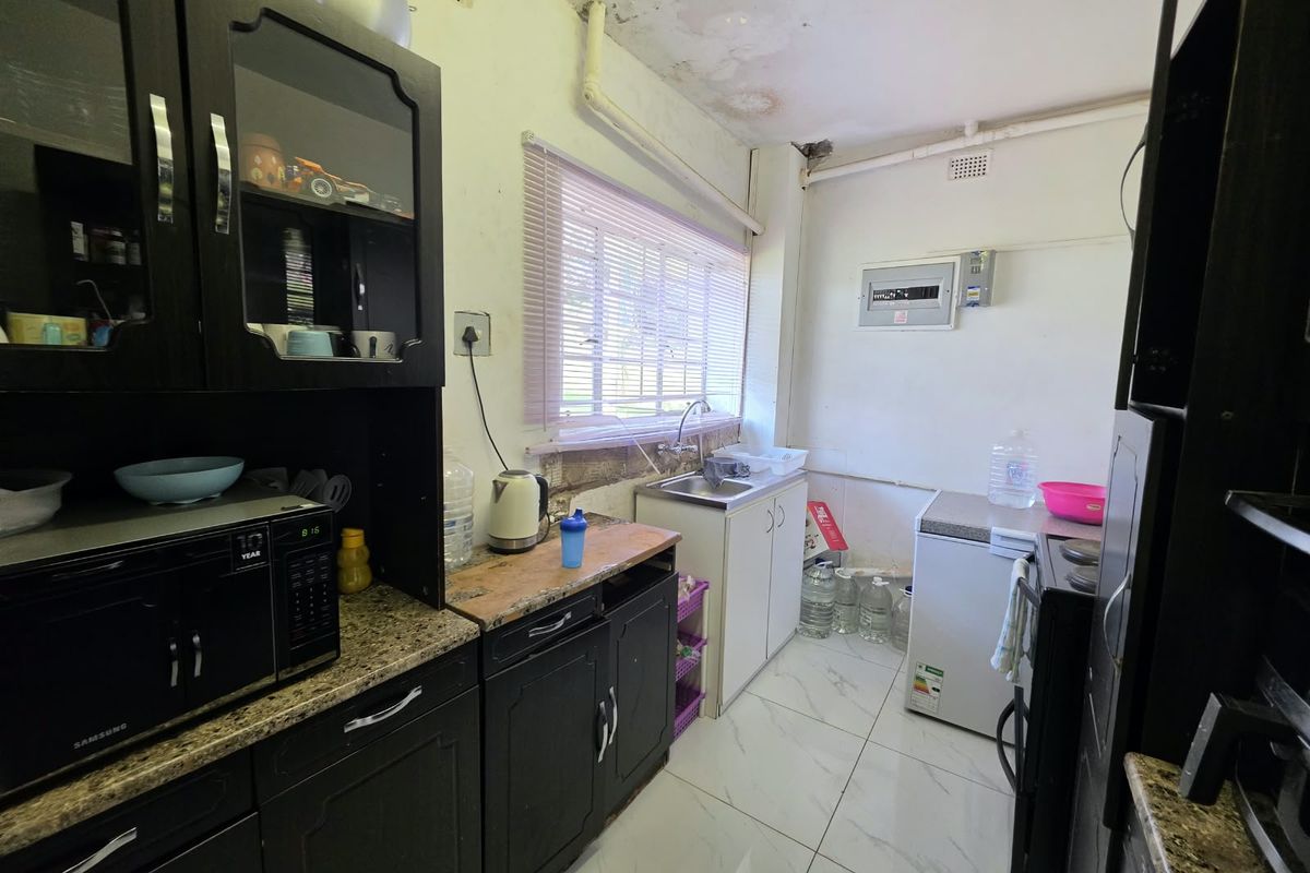 A compact kitchen featuring dark cabinetry, granite countertops, and tiled flooring, currently showing significant signs of ceiling water damage and wall deterioration.