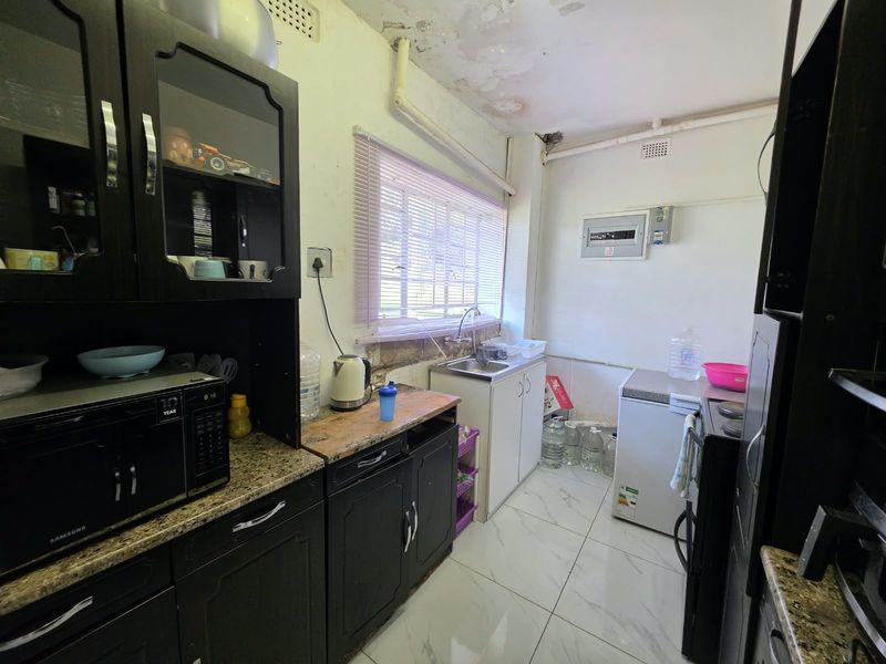 A compact kitchen featuring dark cabinetry, granite countertops, and tiled flooring, currently showing significant signs of ceiling water damage and wall deterioration.