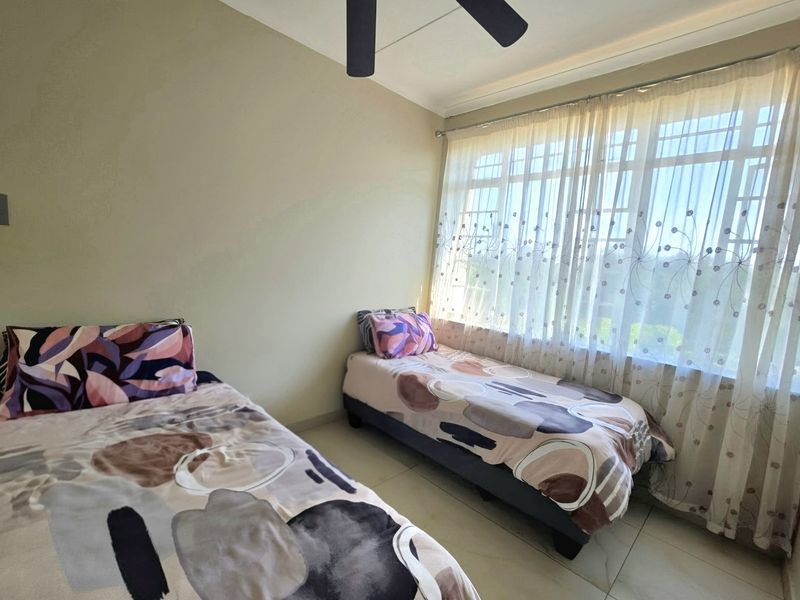 A functional bedroom featuring tiled flooring, a ceiling fan, and a large window with security bars allowing for natural light.