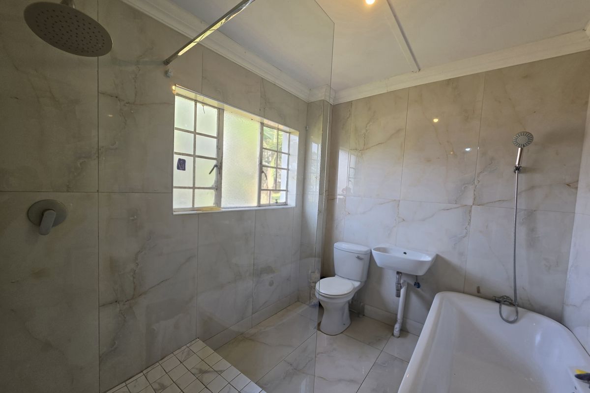 A modern bathroom featuring floor-to-ceiling marble-look tiles, a glass-enclosed rain shower, a freestanding bathtub, and a wall-mounted basin.