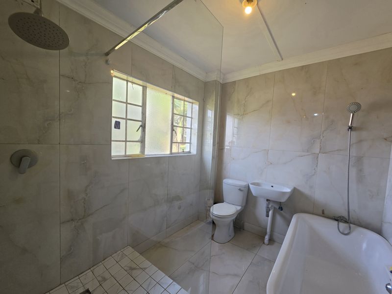 A modern bathroom featuring floor-to-ceiling marble-look tiles, a glass-enclosed rain shower, a freestanding bathtub, and a wall-mounted basin.