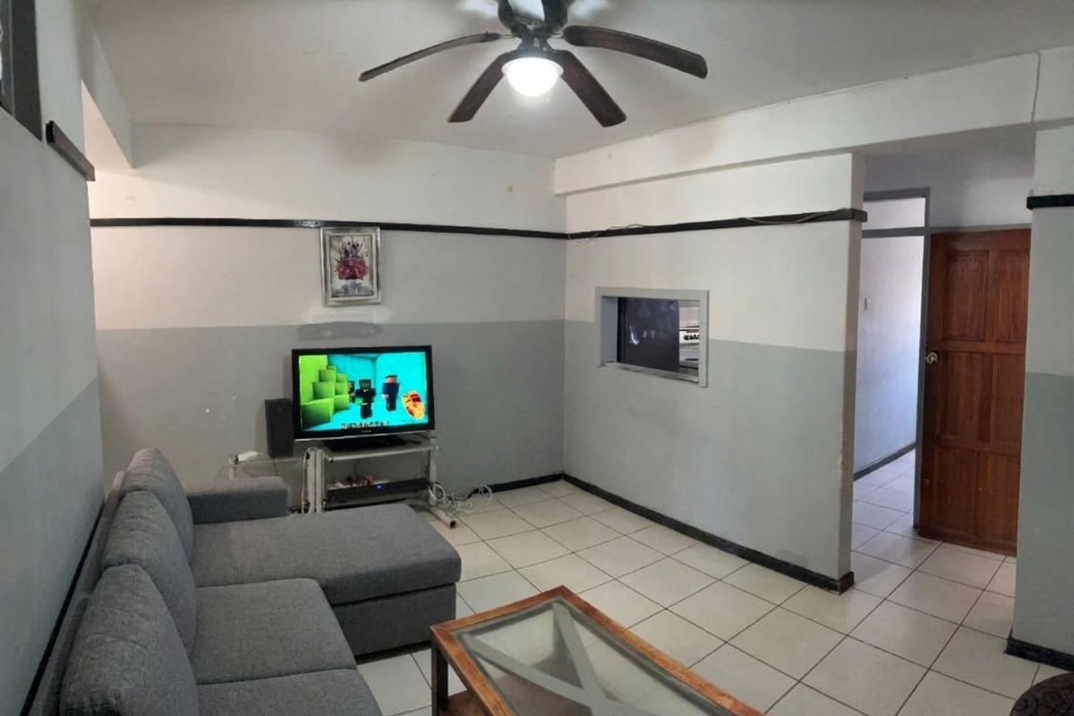 A living room featuring tiled flooring, a ceiling fan, and a pass-through window connecting to the adjacent space.
