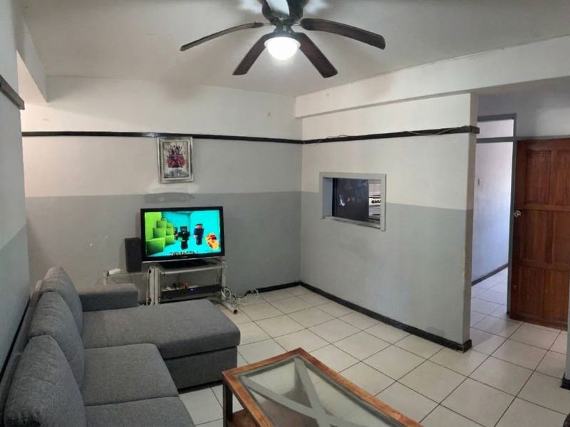 A living room featuring tiled flooring, a ceiling fan, and a pass-through window connecting to the adjacent space.