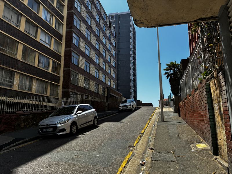 A street-level view of the apartment building exterior, showing the surrounding urban environment, road access, and building facade.