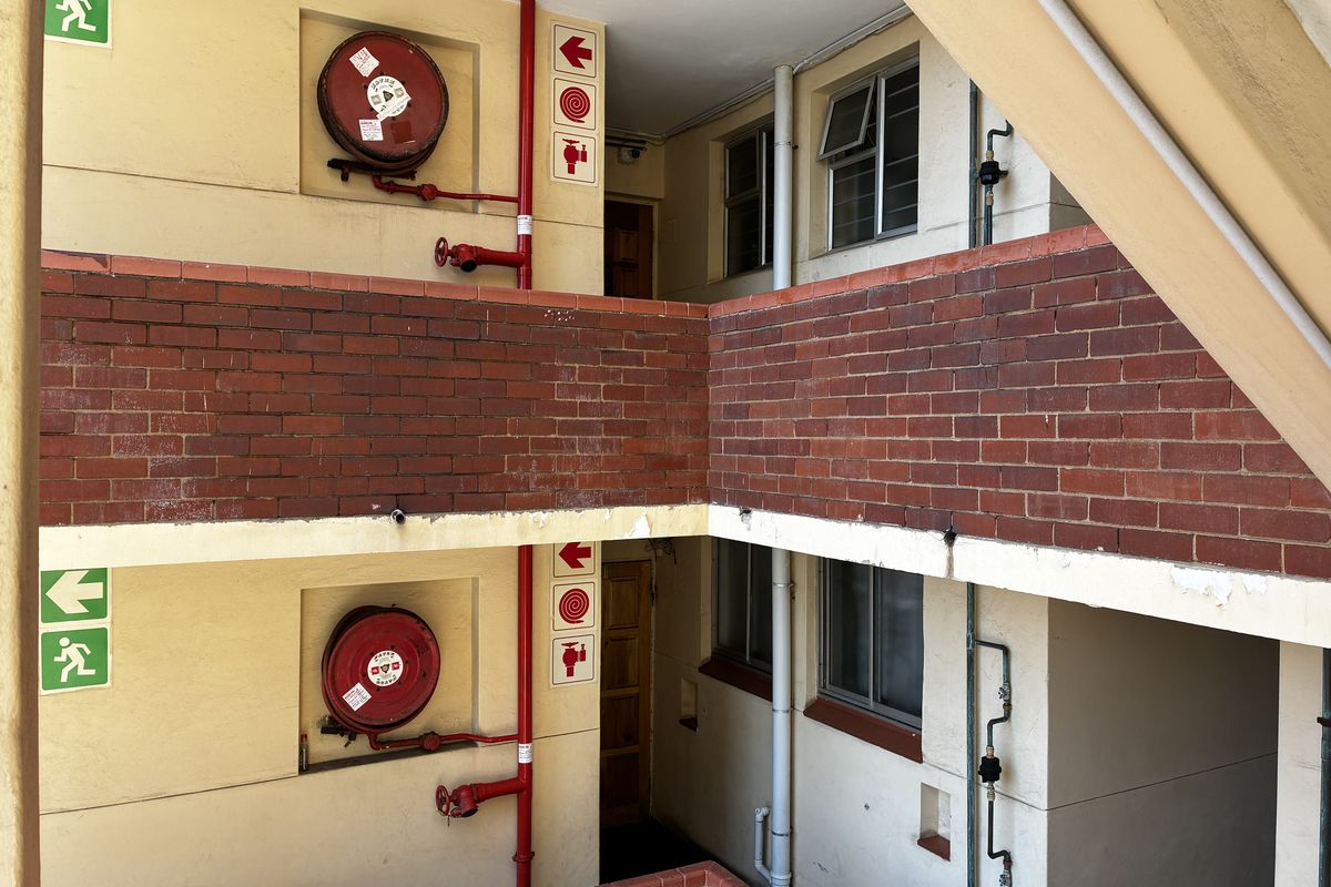 Exterior apartment building hallway featuring brick accents, fire safety equipment, and access to residential units.