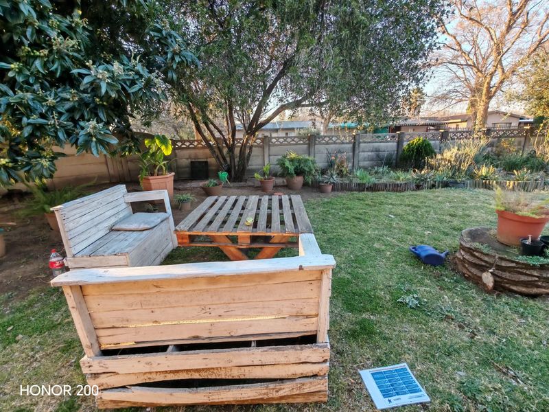 A private backyard garden featuring a lawn, mature trees, and a precast concrete boundary wall.