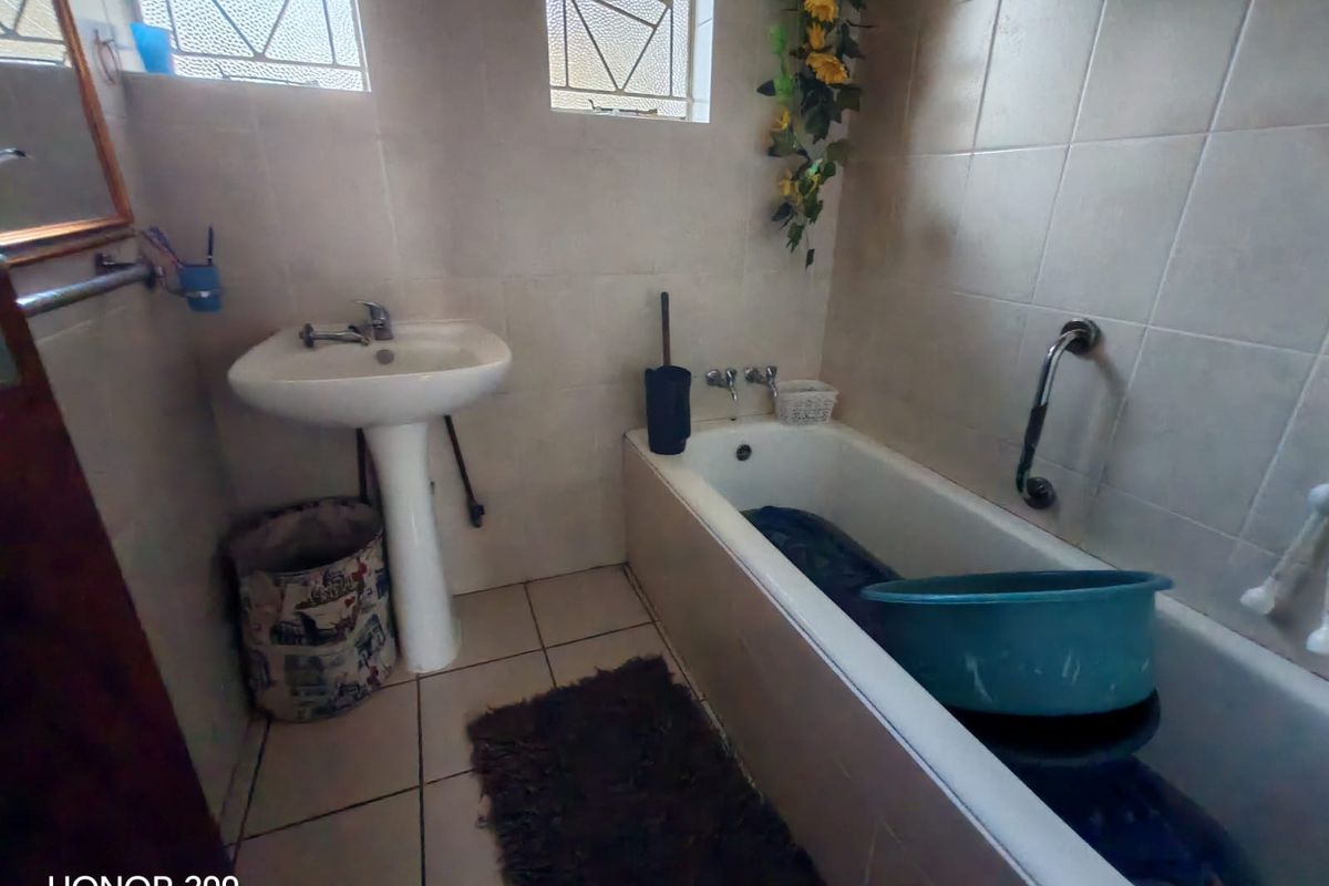 A functional bathroom featuring a pedestal basin, bathtub with grab rail, and tiled finishes, requiring cosmetic updates to improve its overall condition.