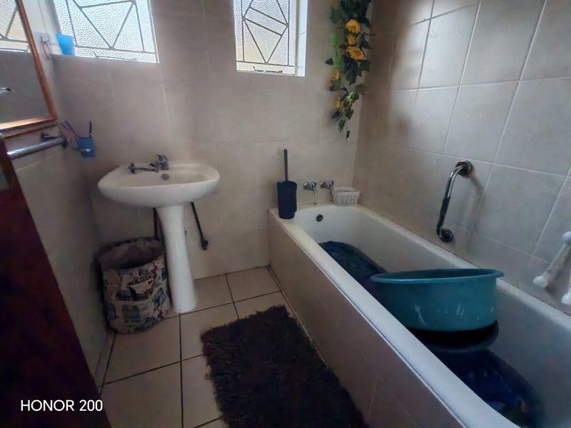 A functional bathroom featuring a pedestal basin, bathtub with grab rail, and tiled finishes, requiring cosmetic updates to improve its overall condition.