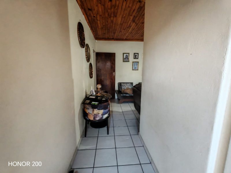 A narrow hallway featuring ceramic floor tiles and a wooden tongue and groove ceiling, leading into an adjacent living space.