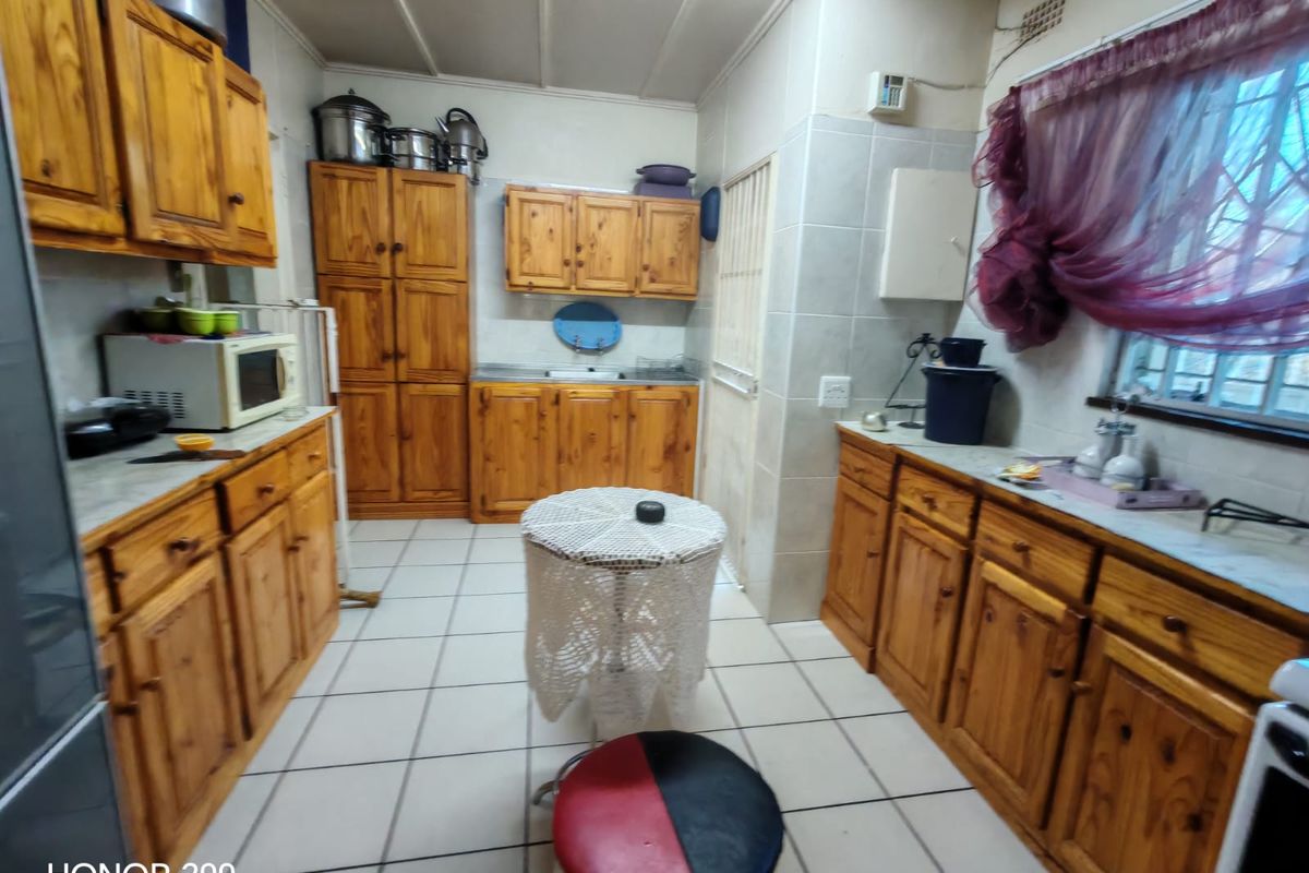 A functional kitchen featuring extensive wooden cabinetry, tiled flooring, and a tiled splashback, offering ample storage and workspace.