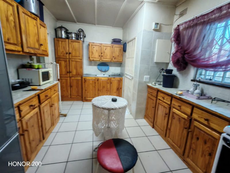 A functional kitchen featuring extensive wooden cabinetry, tiled flooring, and a tiled splashback, offering ample storage and workspace.