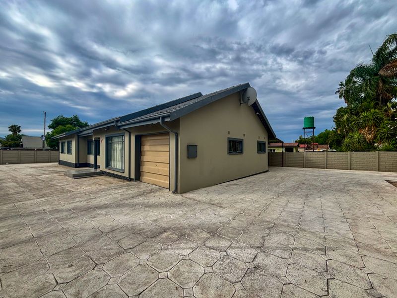 Exterior view of a single-story house featuring a paved driveway, integrated garage, and secure precast boundary walling.