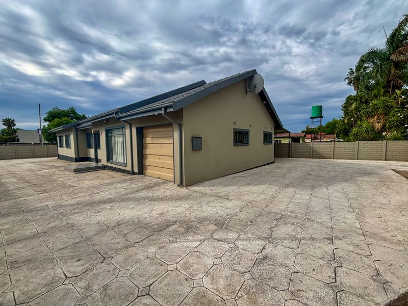 A well-maintained single-story house featuring a paved driveway, integrated garage, and secure boundary walling with an external water tank.