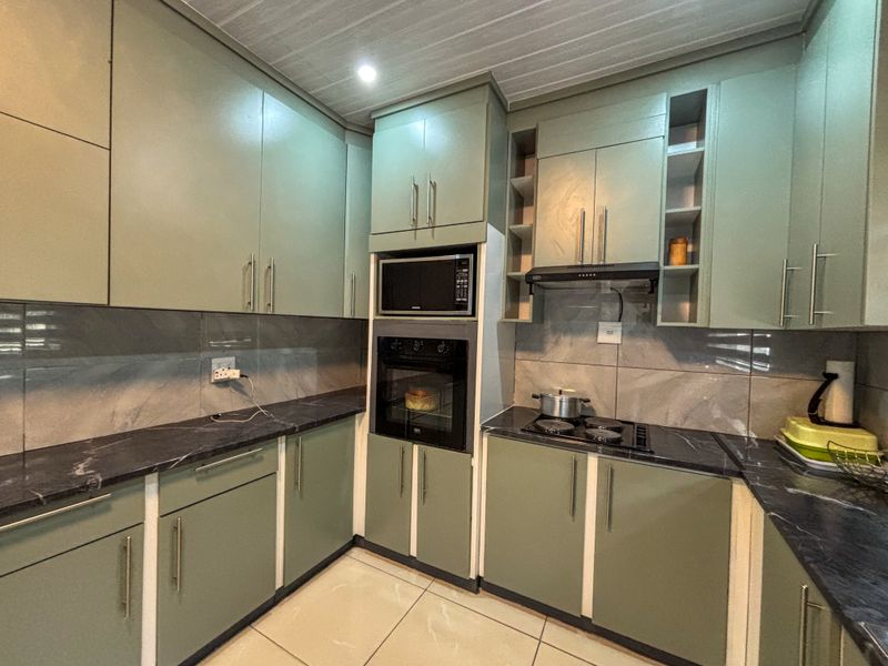 Modern kitchen featuring sage green cabinetry, dark marble-effect countertops, built-in oven, microwave, and electric hob with a sleek tiled backsplash.