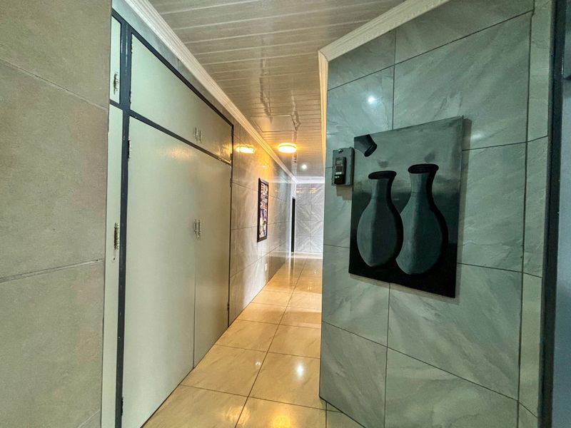 A well-lit hallway featuring tiled flooring and walls, with built-in storage cupboards and an integrated intercom system.