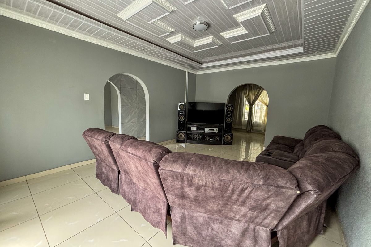 A living room featuring tiled flooring, decorative ceiling panels, and arched doorways leading to adjacent spaces.