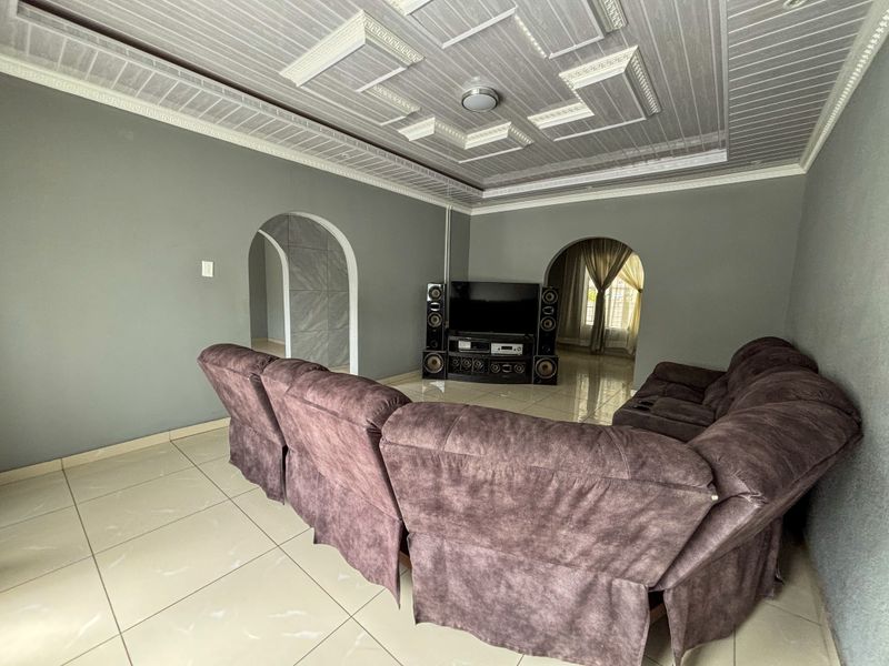 A living room featuring tiled flooring, decorative ceiling panels, and arched doorways leading to adjacent spaces.