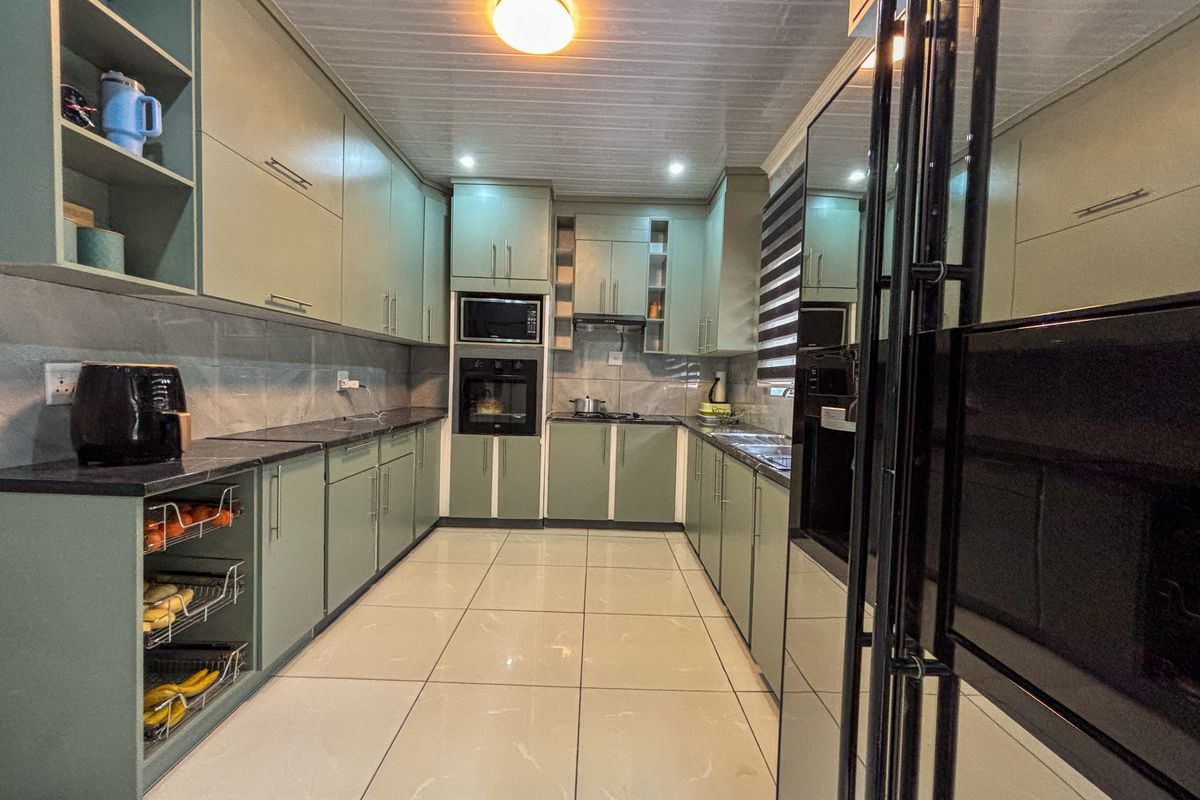A modern, well-maintained kitchen featuring sage green cabinetry, stone countertops, tiled flooring, and integrated appliances including an oven and microwave.